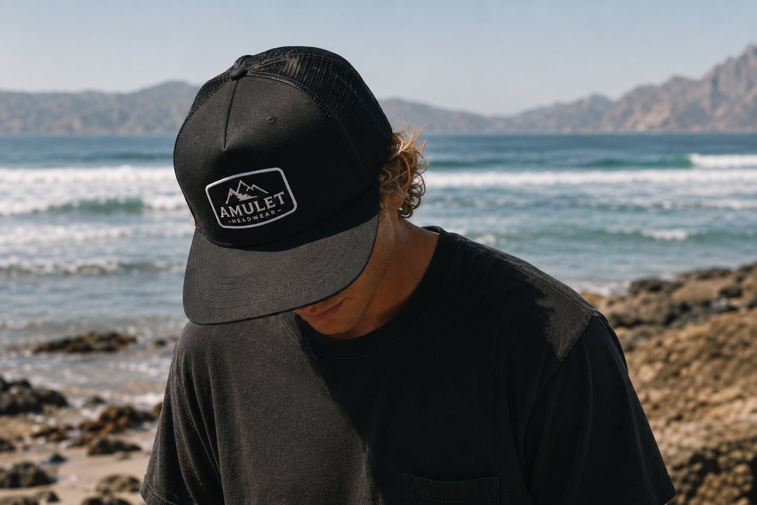 Person in black Amulet trucker cap on a coastal morning